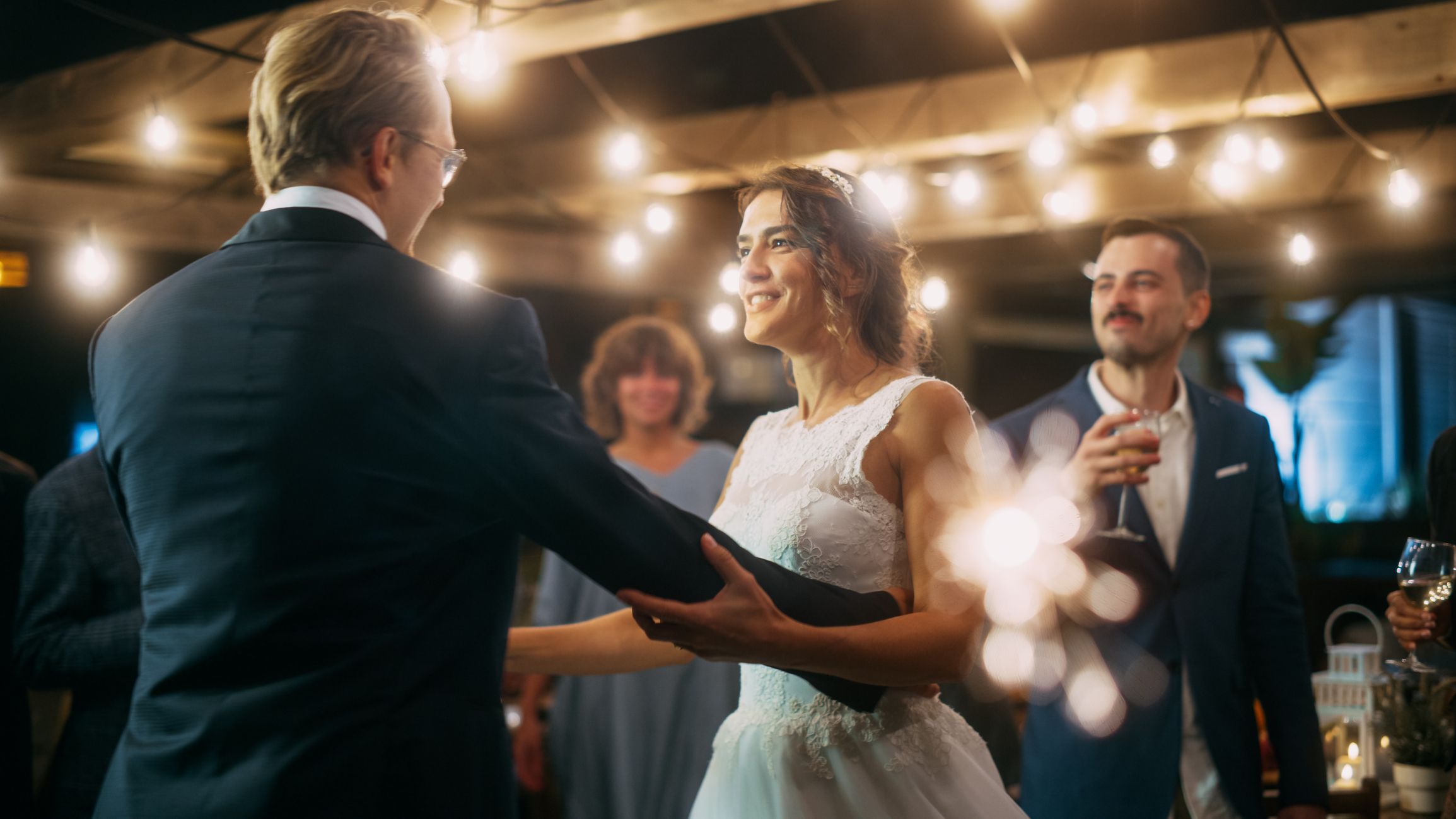 Beautiful Bride in White Dress and Groom in Stylish Black Suit Celebrate Wedding at an Evening Reception Party. Newlyweds Dancing at a Venue with Best Multiethnic Diverse Friends.