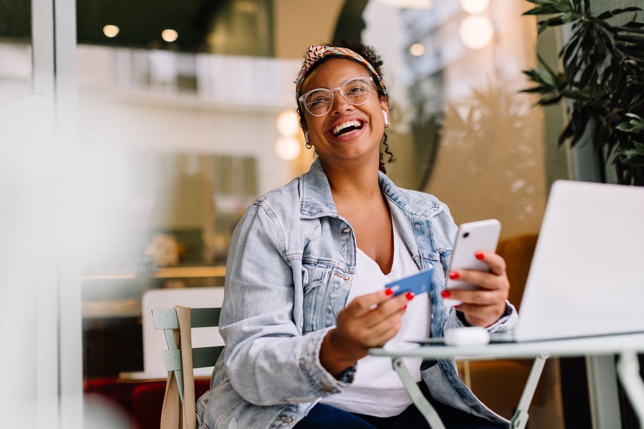 Young woman uses smartphone and laptop at cafe for work