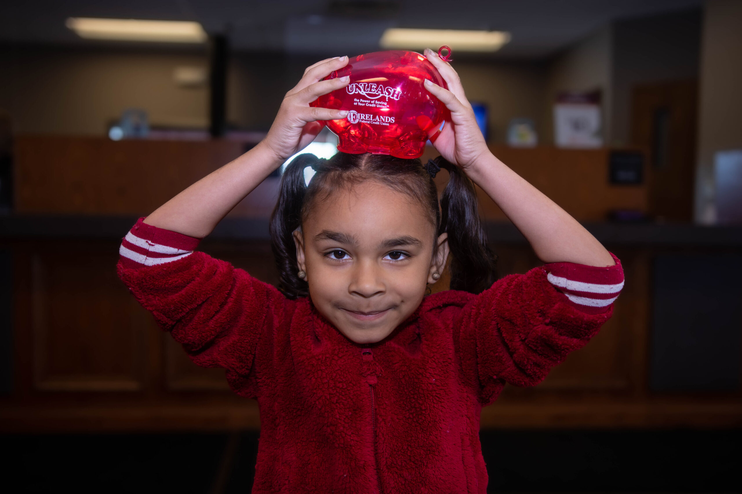 Little girl holding a Firelands piggy bank on her head